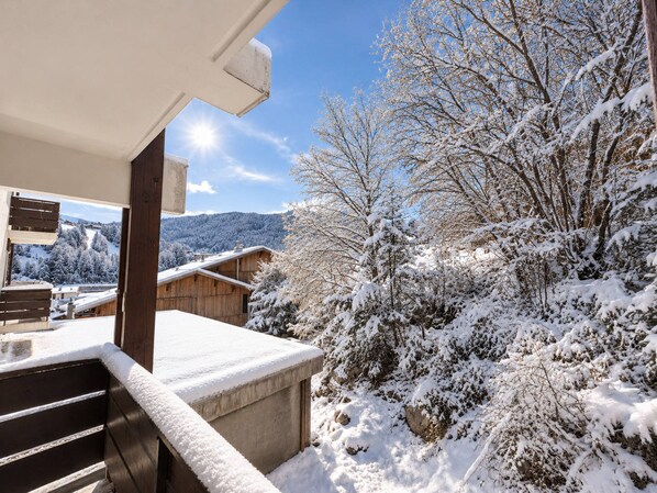 Un balcón cubierto de nieve con vistas a una cabaña de madera y árboles cargados de nieve.