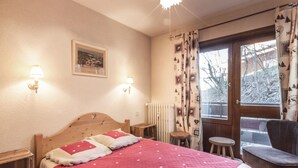 Een slaapkamer met een houten bed, twee bedlampjes, een ingelijst schilderij aan de muur, een raam met gordijnen en een stoel bij het raam.