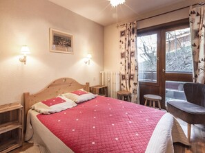 Une chambre avec un lit en bois, deux lampes de chevet, un tableau encadré au mur, une fenêtre avec des rideaux et une chaise près de la fenêtre.