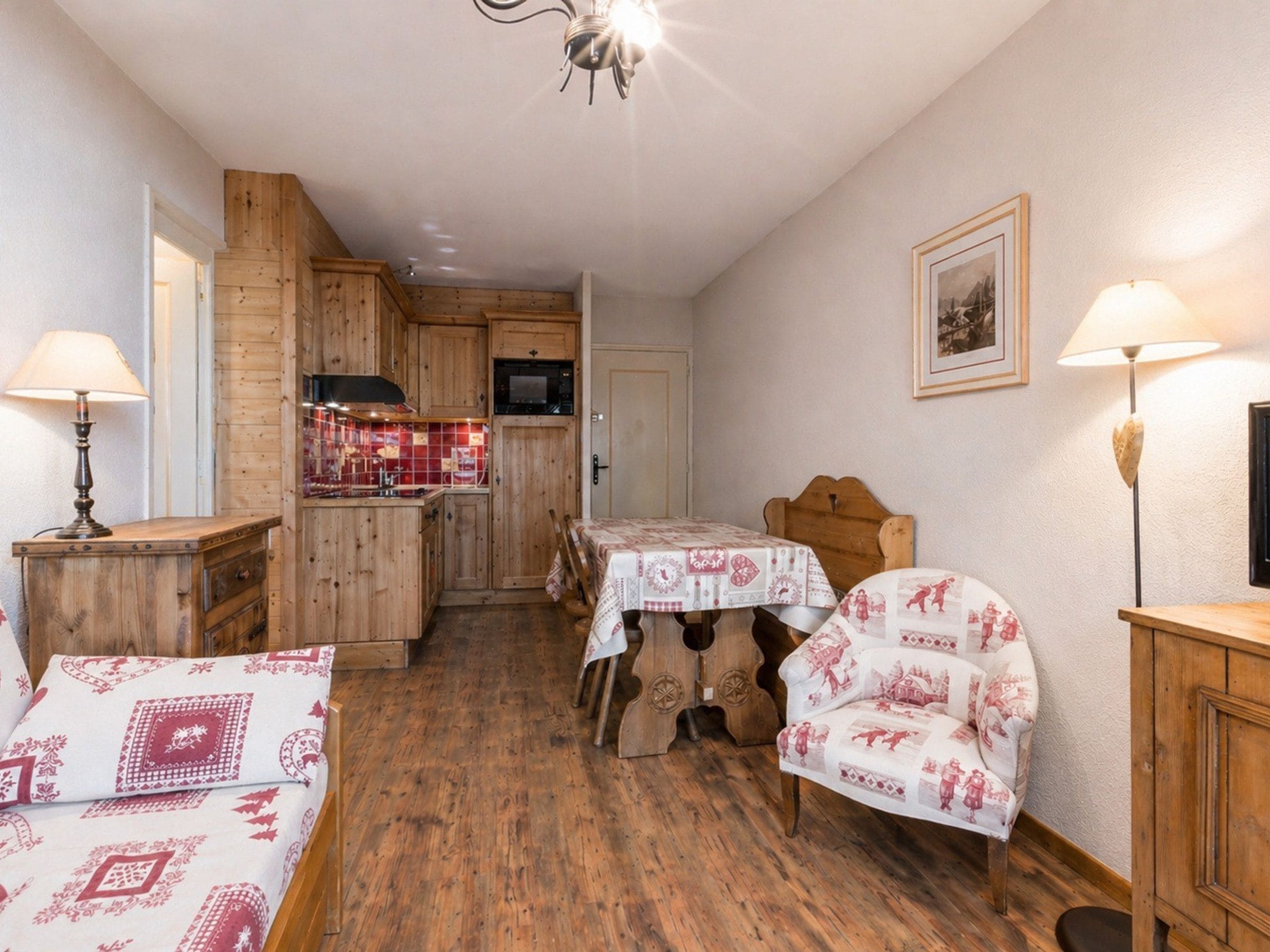 Un cuarto acogedor con piso de madera, una mesa de comedor con sillas, una cocina con armarios de madera y una lámpara en el techo.