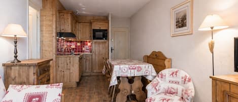 Un cuarto acogedor con piso de madera, una mesa de comedor con sillas, una cocina con armarios de madera y una lámpara en el techo.