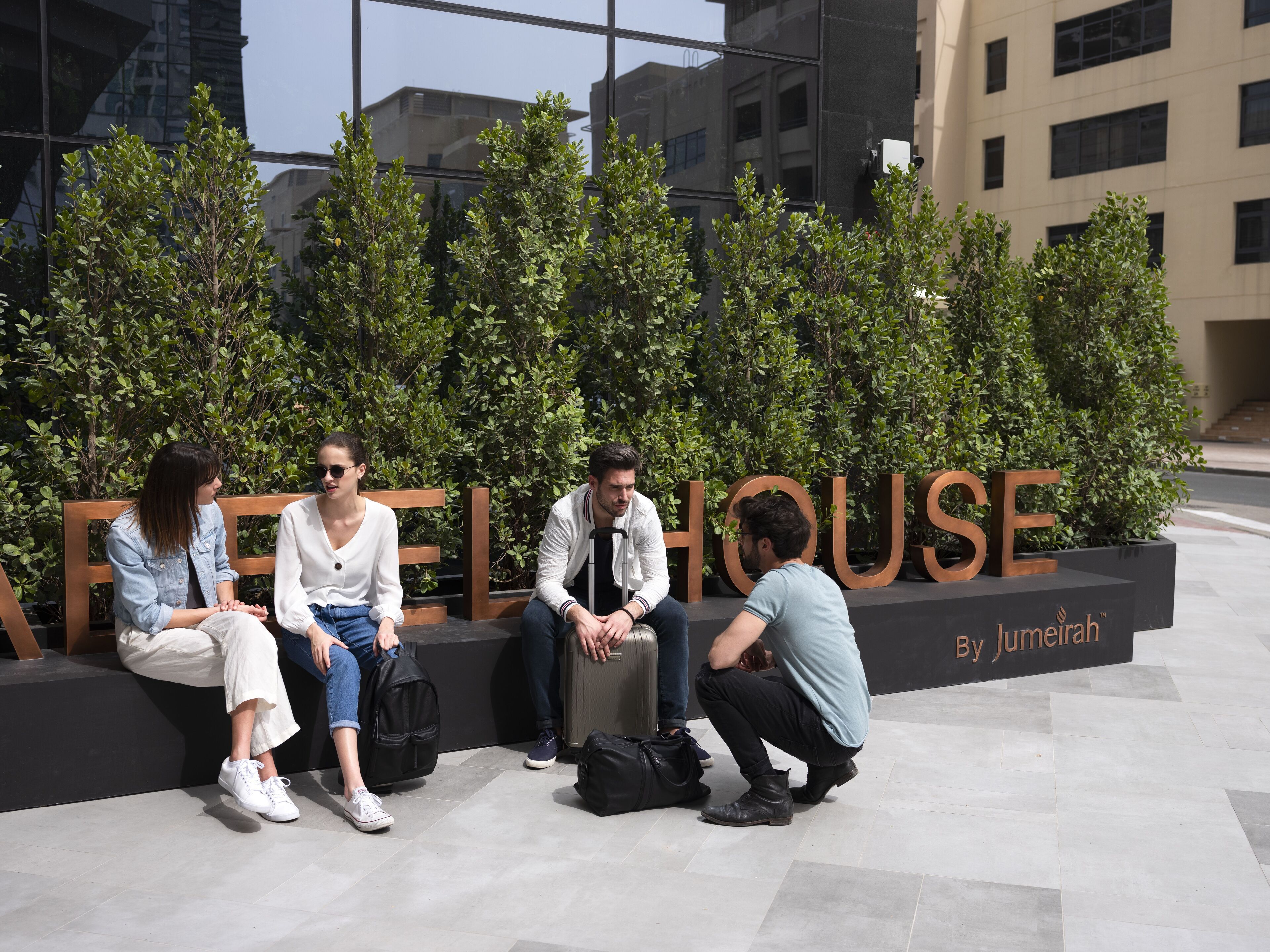 A group of people sitting on a bench in front of a building with the sign "Jumeirah House".