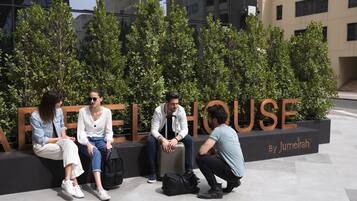 A group of people sitting on a bench in front of a building with the sign "Jumeirah House".