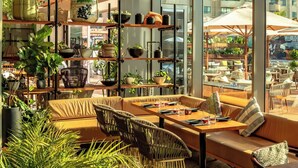 Un área de estar moderna al aire libre con mobiliario de mimbre, estantes con plantas y vista a la ciudad.
