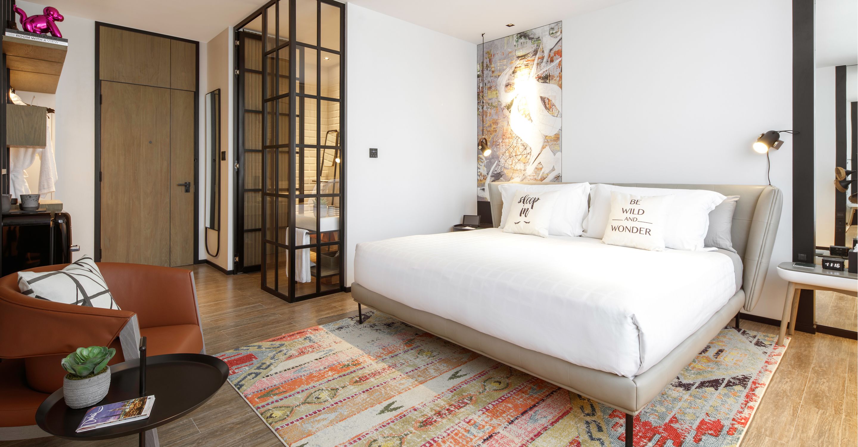 Una habitación de hotel moderna con una cama grande, un sofá, una mesita y un tapete decorativo.