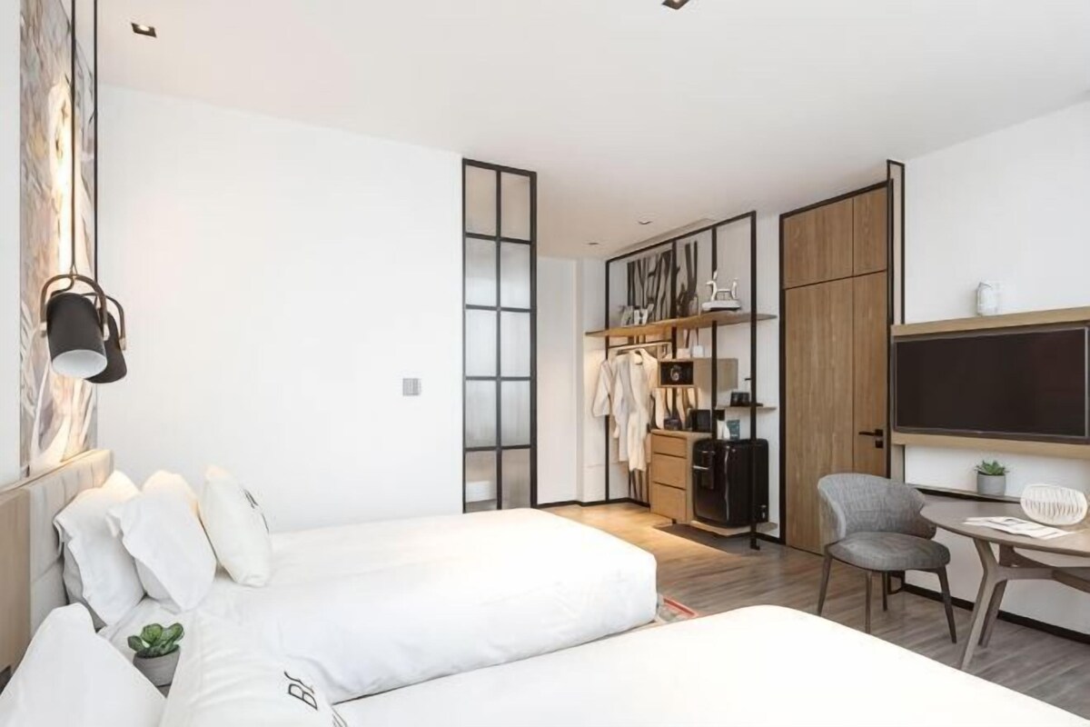 Une chambre d’hôtel moderne équipée d’un lit, d’une table de chevet et d’un petit bureau avec une chaise.