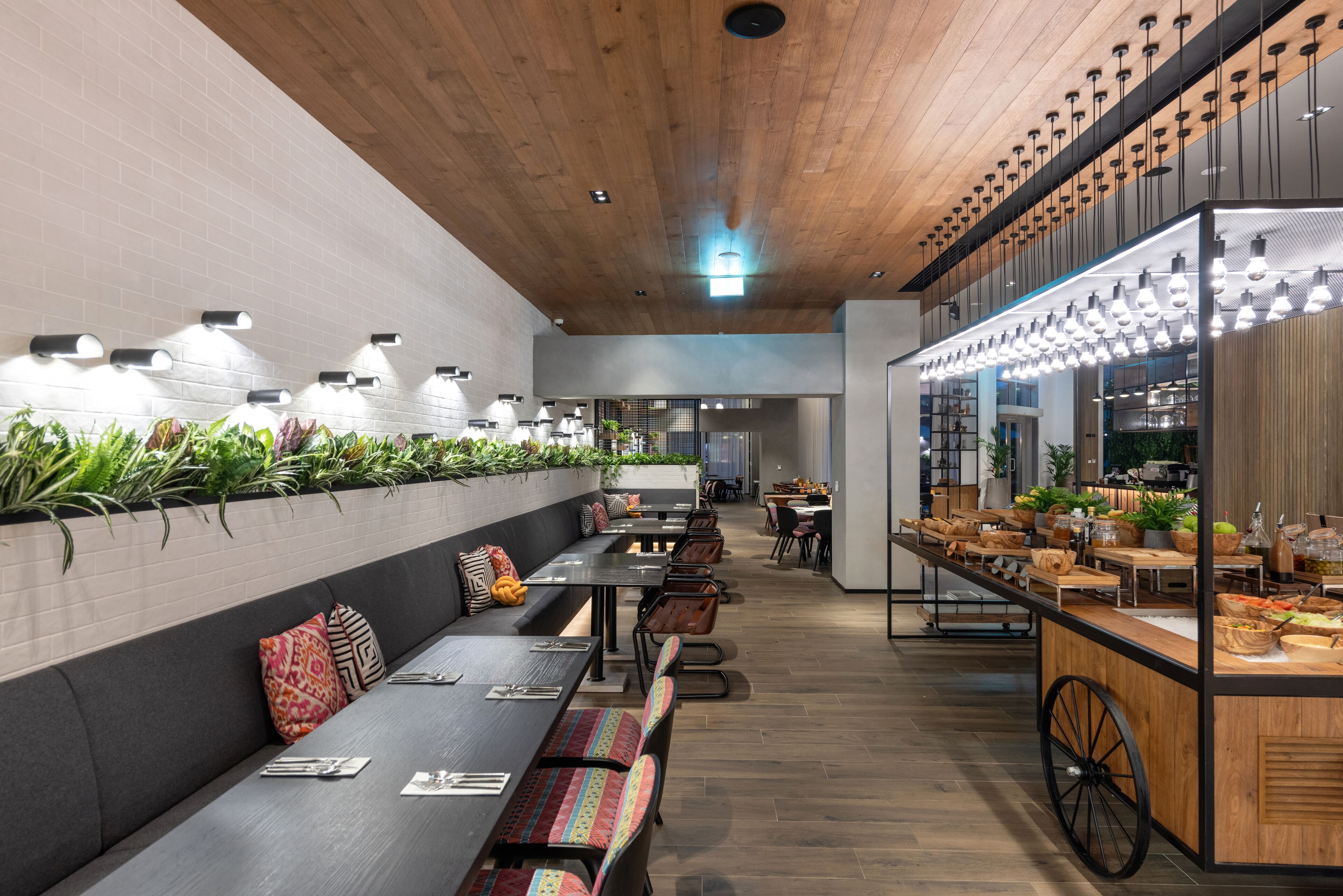 Un restaurante moderno con mesas comunitarias largas, una zona de bar con exhibiciones de comida y un techo de madera.