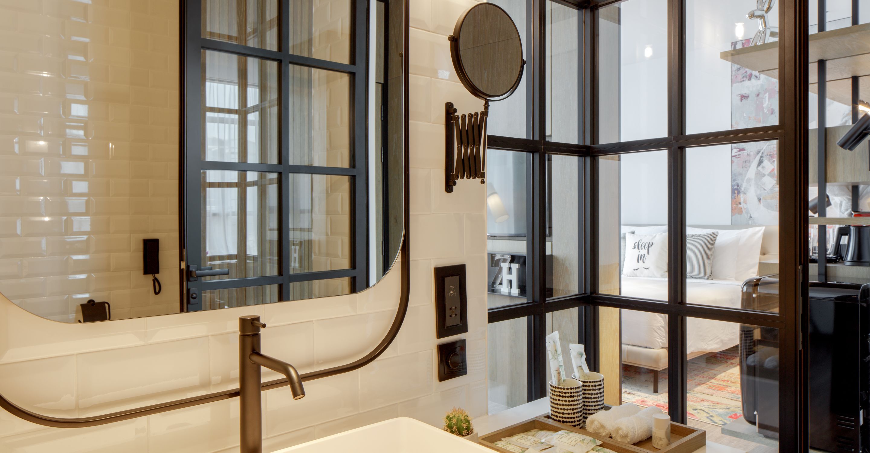 A modern bathroom with a large mirror, a bathtub, and a window with a view of a living room.