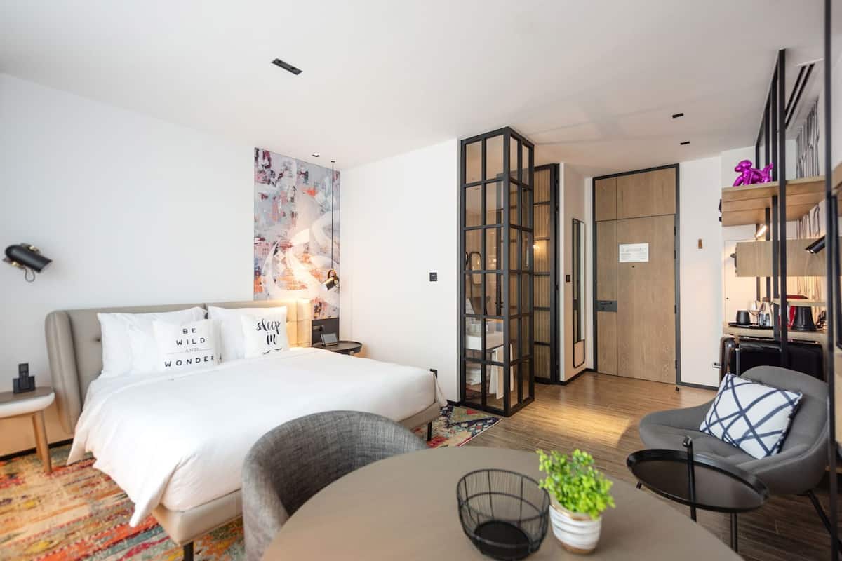 Una habitación de hotel moderna con cama, escritorio, silla, una mesita y una planta en maceta.