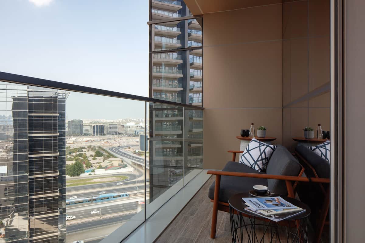 Un balcón moderno con vista a la ciudad, un sofá, una mesa con una revista y una planta pequeña en el alféizar.