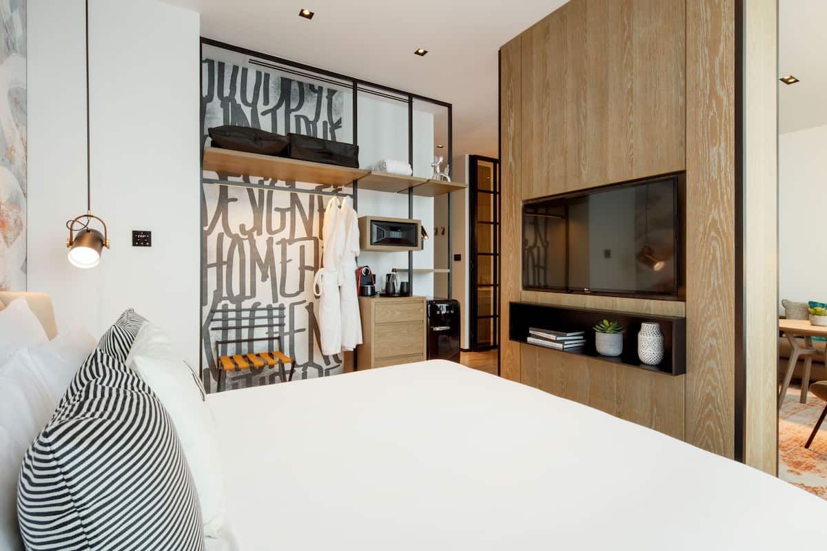 Un dormitorio moderno con una cama grande, un televisor montado en la pared, un armario empotrado y una cafetera.