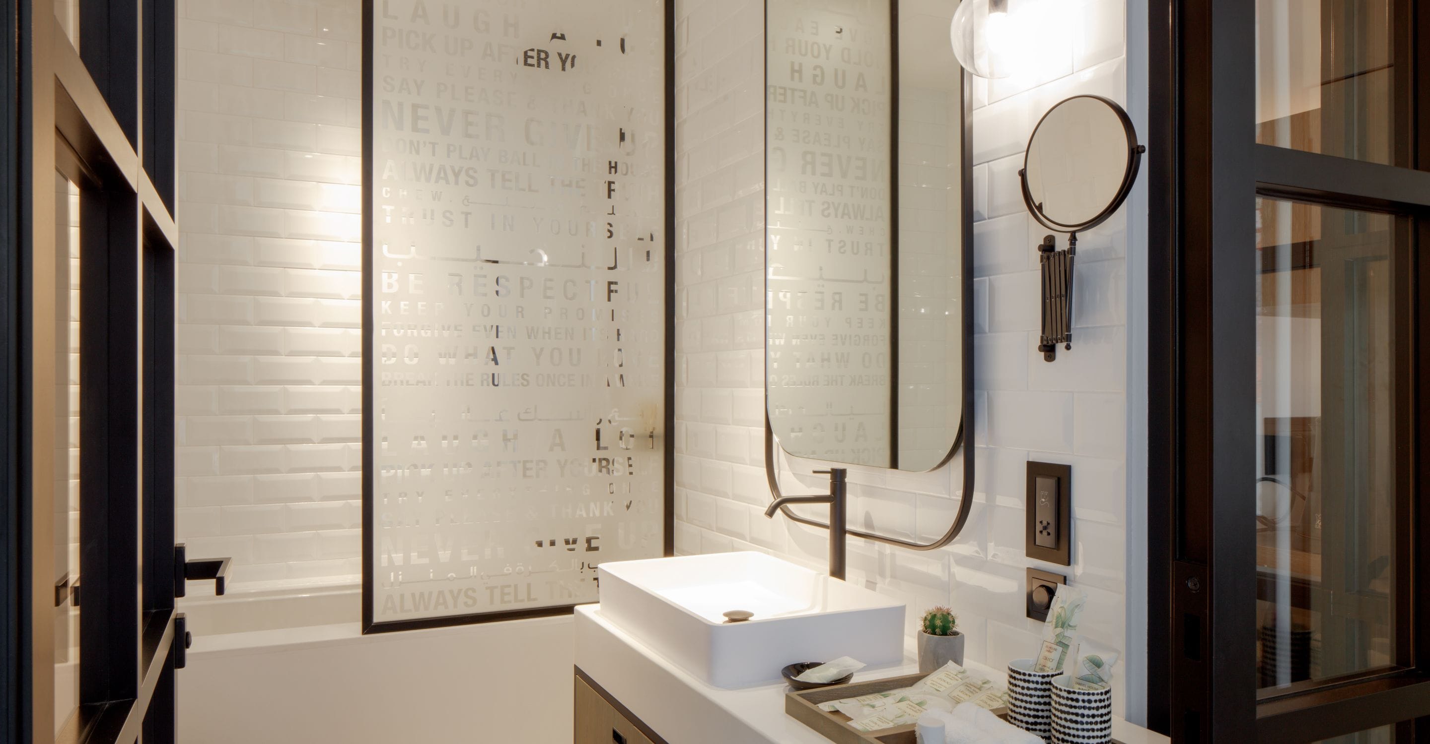 Un baño moderno con un lavabo blanco, un espejo grande y una pared con citas motivacionales.