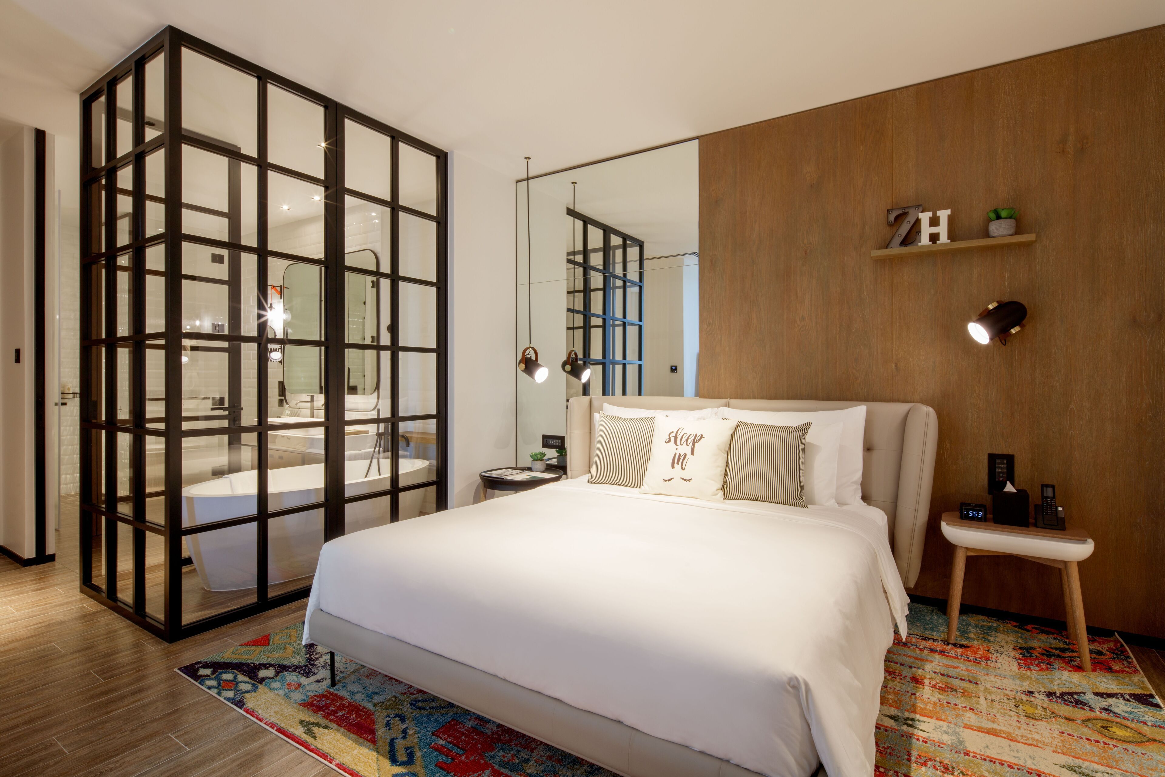 Un dormitorio moderno con una cama grande, un separador de vidrio, una pared de madera, un estante pequeño y una mesita de noche.