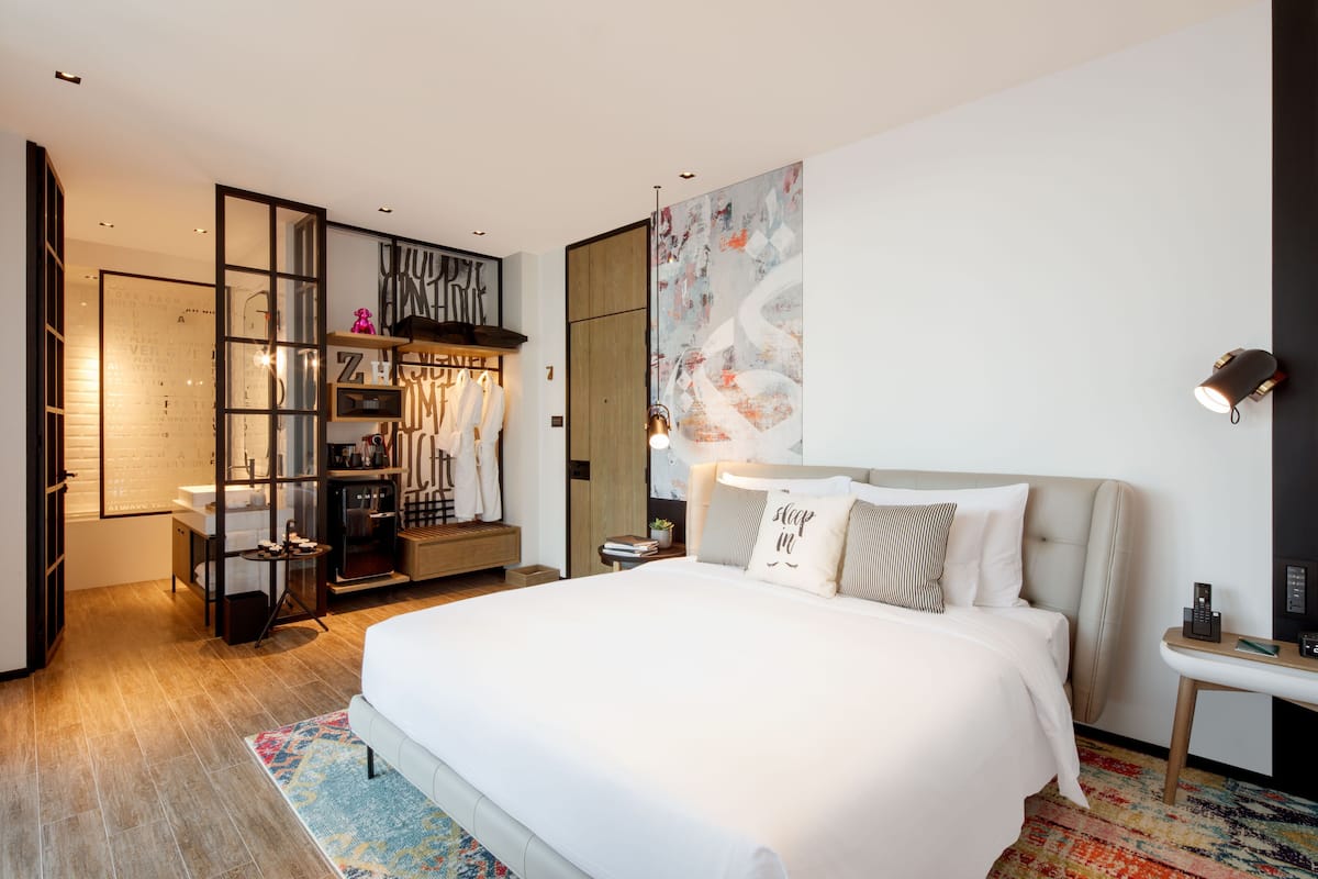 Una habitación de hotel moderna con una cama grande, un armario, un escritorio y un cuadro abstracto de gran tamaño en la pared.
