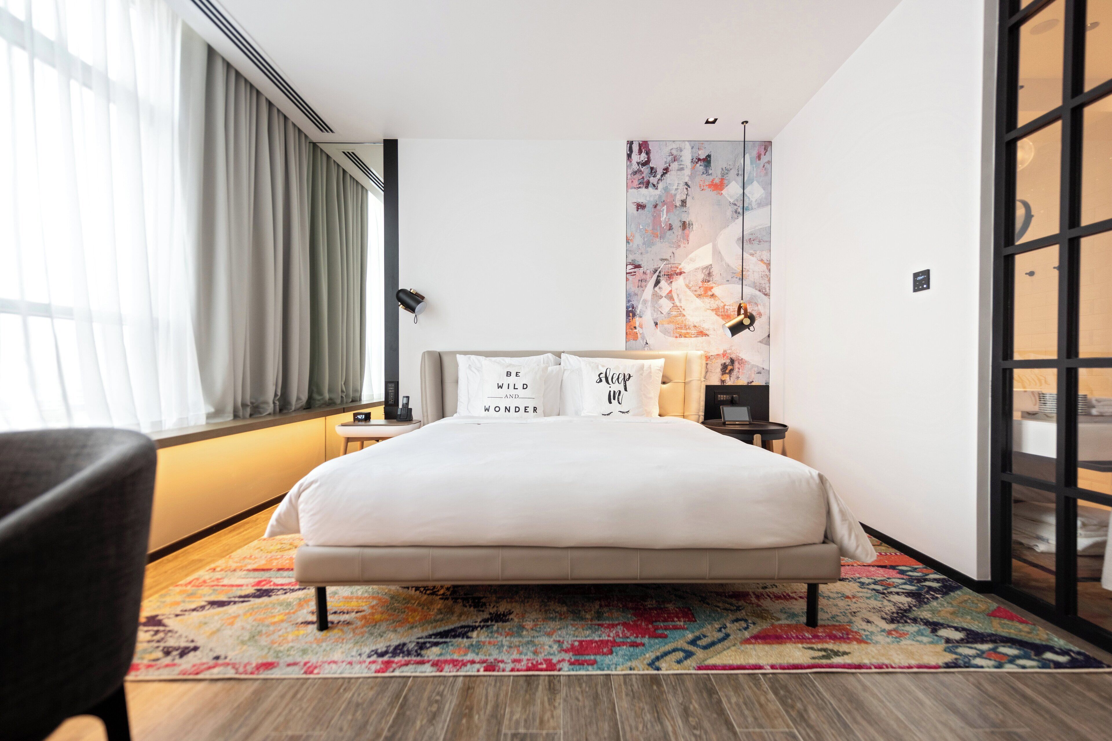 A modern hotel room with a large bed, a nightstand, a desk, and a chair.