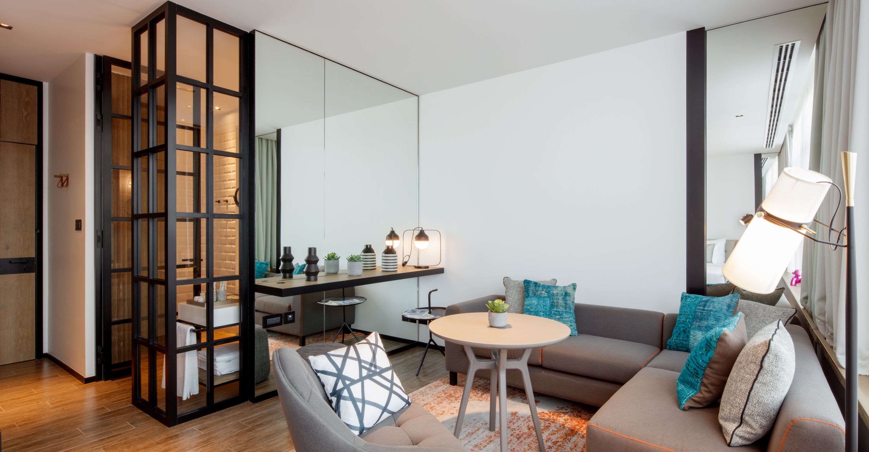 Uma sala de estar moderna com sofá, mesa de jantar e área de cozinha visível através de um painel de vidro.