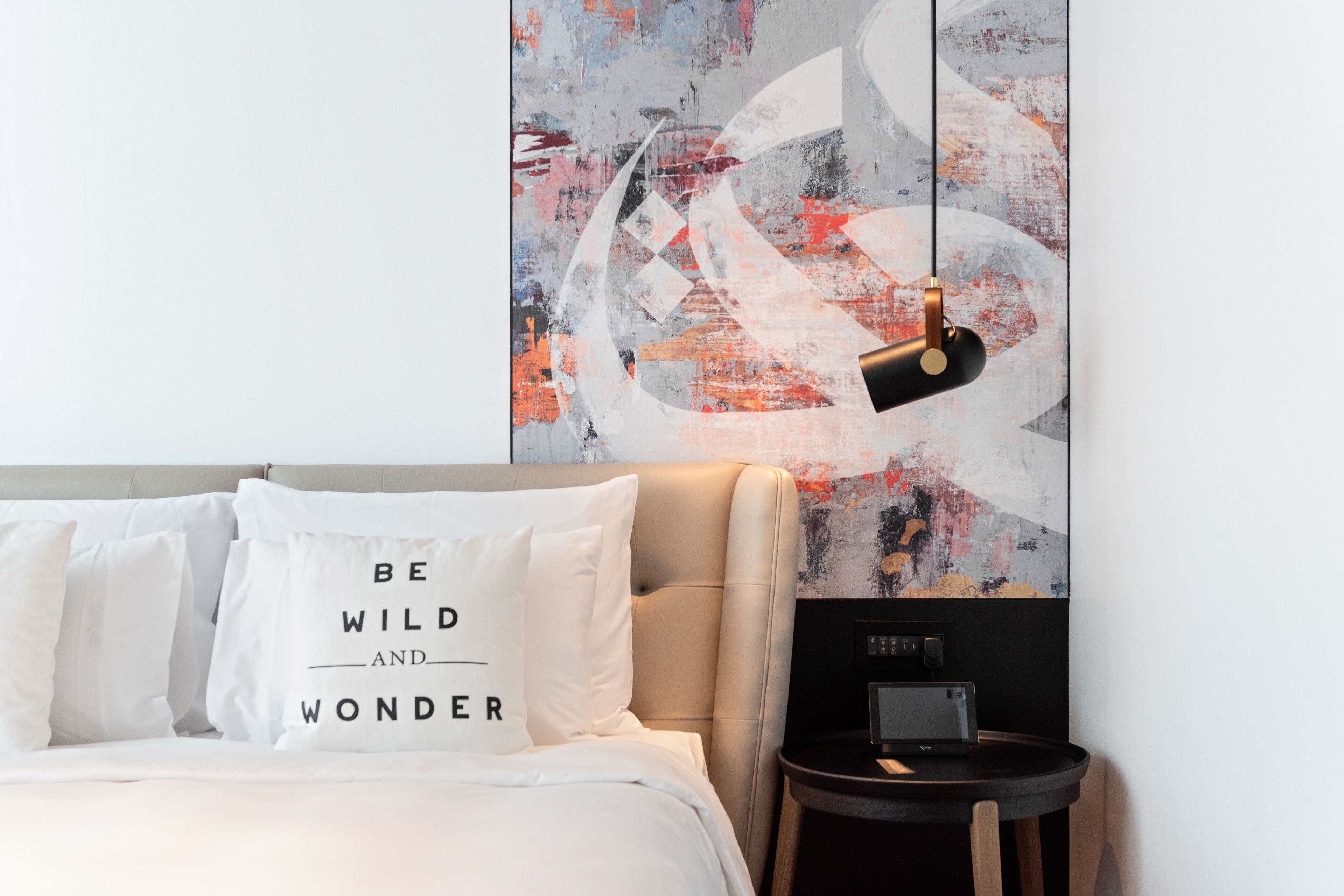 Een moderne slaapkamer met een bed, witte kussens, een zwart nachtkastje en een groot abstract schilderij aan de muur.
