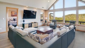 Amplia sala de estar con un sofá modular grande, un televisor de pantalla plana y un balcón con vistas al exterior.
