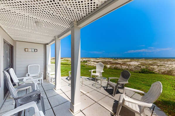 Relax in comfort with a view of the beach from this outdoor seating area, featuring Adirondack chairs and a small table.