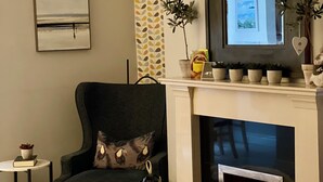 A cozy living room with a fireplace, a comfortable armchair, a small side table, and a decorative pillow. - Elegant  townhouse steps from historic Birr Castle Demense  (Birr)