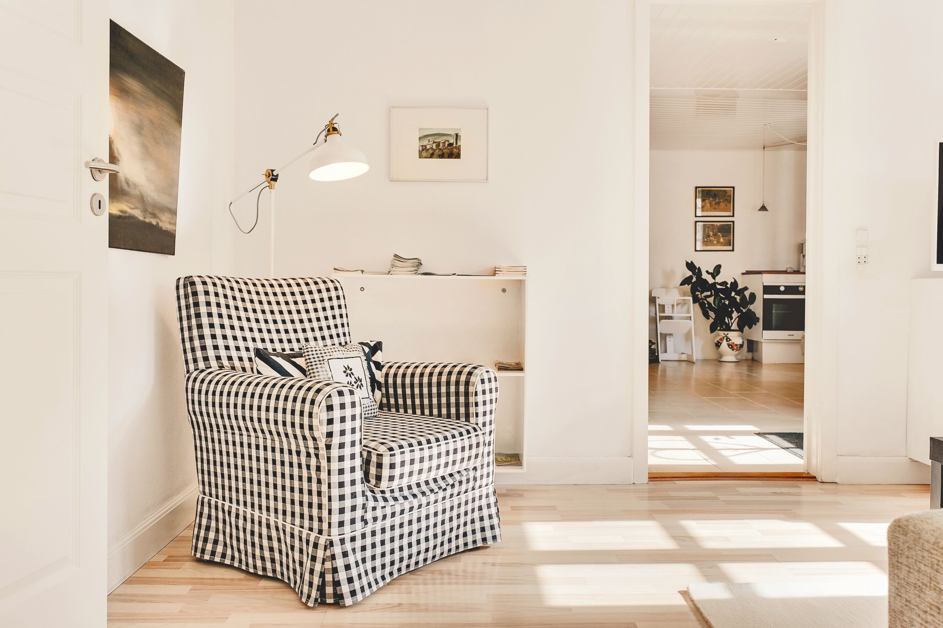 A checkered armchair in a bright room with a white door, a framed picture, and a pendant light.