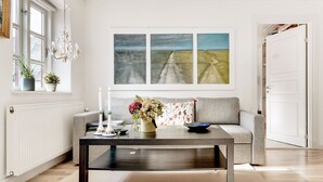 A modern living room with a grey sofa, a dark wooden coffee table, and a large window with three paintings. - Bed and Breakfast Åløkke (Nyborg)