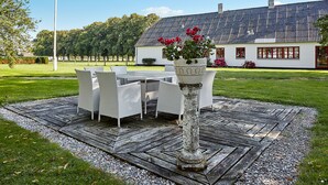 A patio with a table and chairs, a decorative planter with flowers, and a white house in the background. - Bed and Breakfast Åløkke (Nyborg)