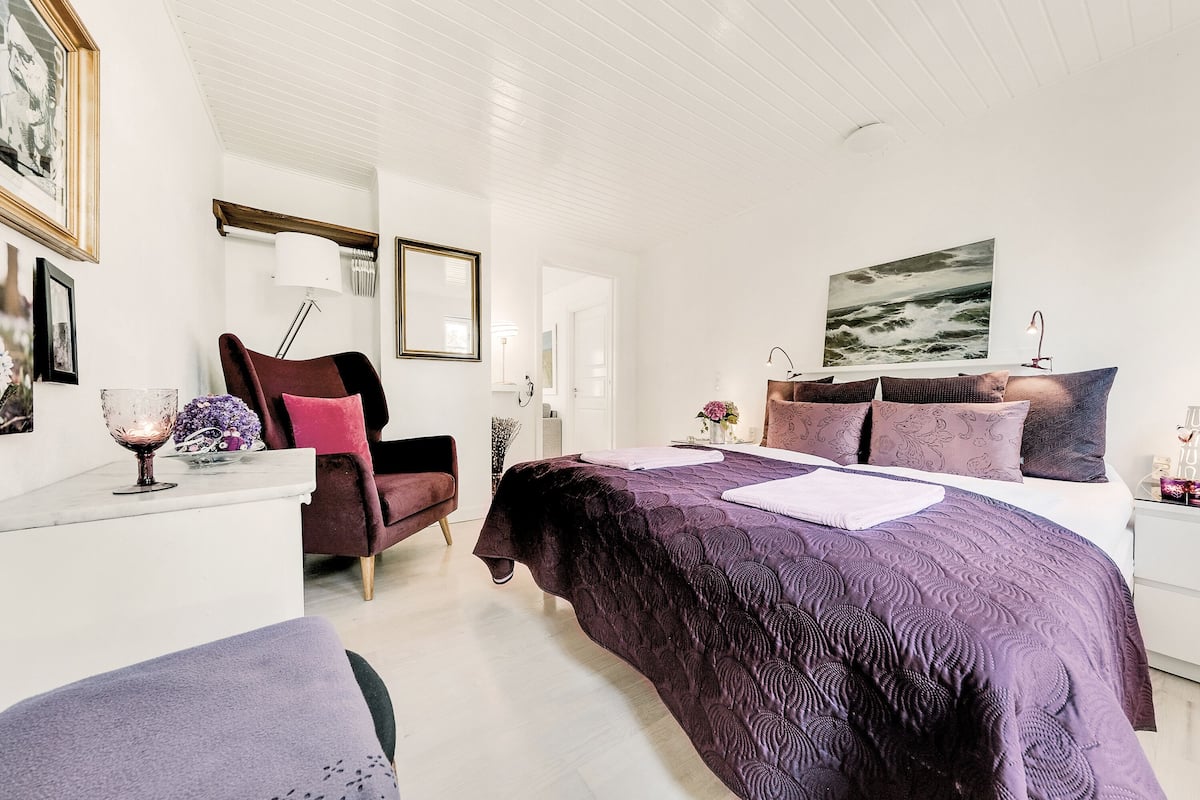 A bedroom with a large bed, a chair, a desk, and a lamp.