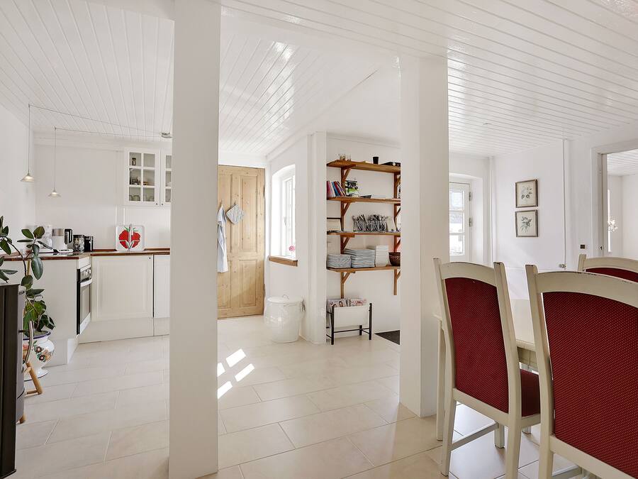 A spacious kitchen with white cabinets, a wooden door, and a dining area with white chairs and a red tablecloth.