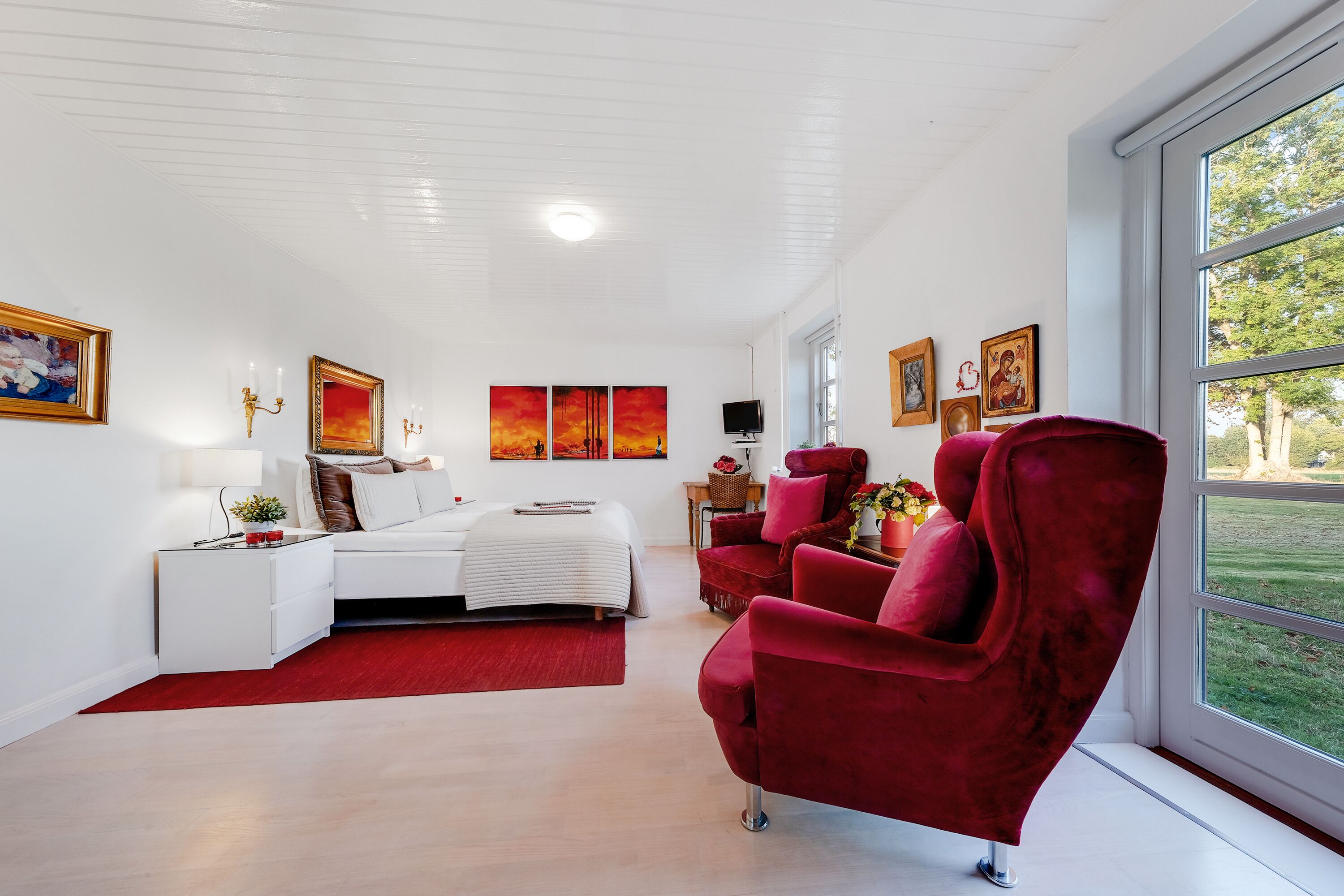 A modern bedroom with a bed, a red armchair, and artwork on the walls.