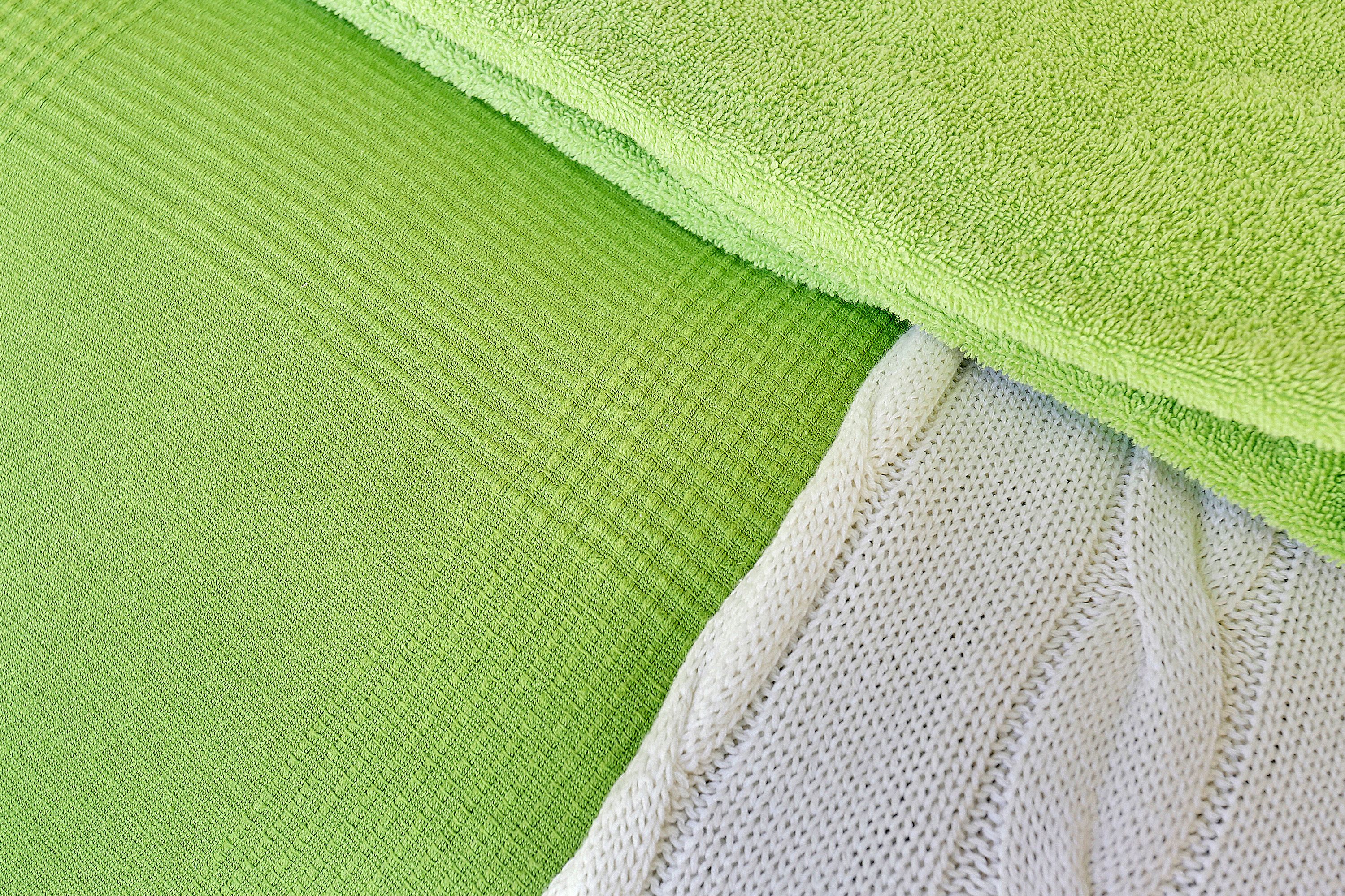 A close-up of a green textured fabric and a white knitted fabric.