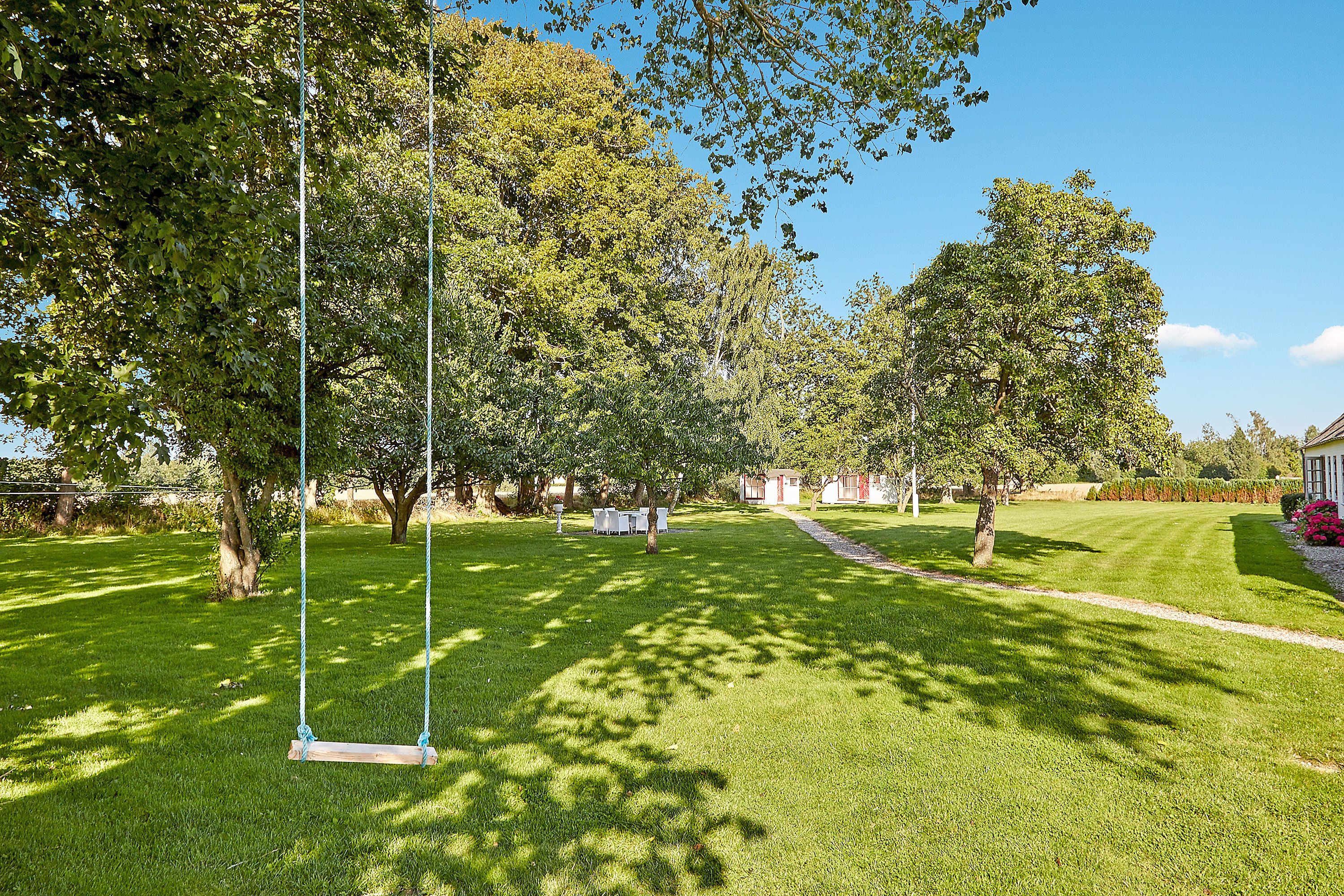 A well-maintained grassy area with a swing set, trees, and a clear sky.