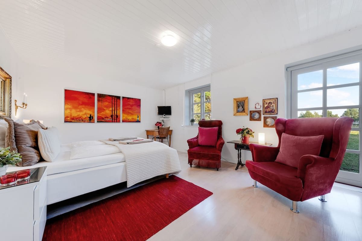 A modern bedroom with a bed, a red armchair, and artwork on the walls.