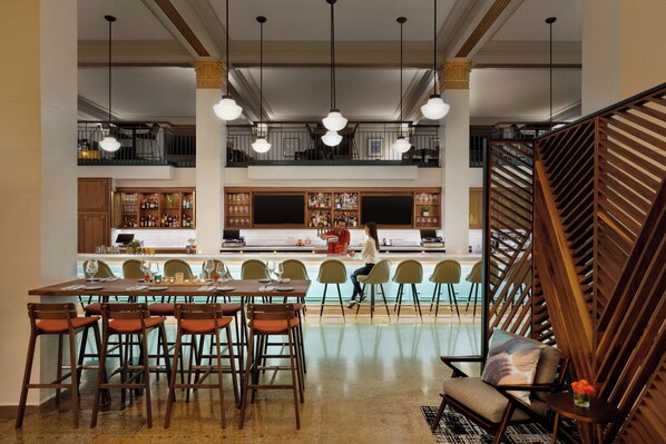 Un comedor amplio con una mesa larga y numerosas sillas, una zona de bar con taburetes, y una escalera con barandillas de madera.