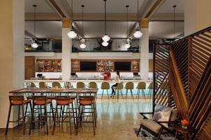 Un comedor amplio con una mesa larga y numerosas sillas, una zona de bar con taburetes, y una escalera con barandillas de madera.