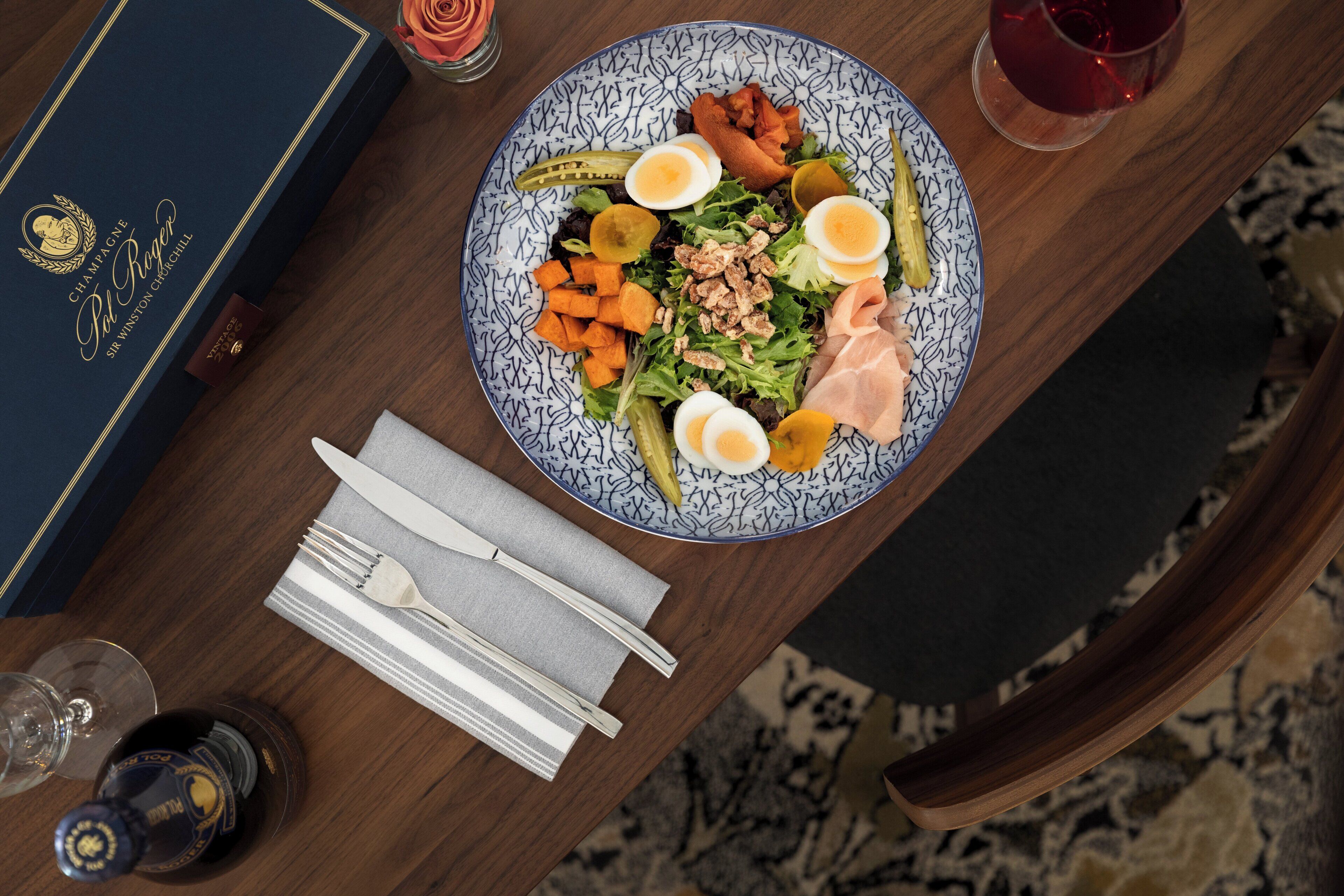A dining table with a plate of food, a bottle of wine, a glass, and a book.