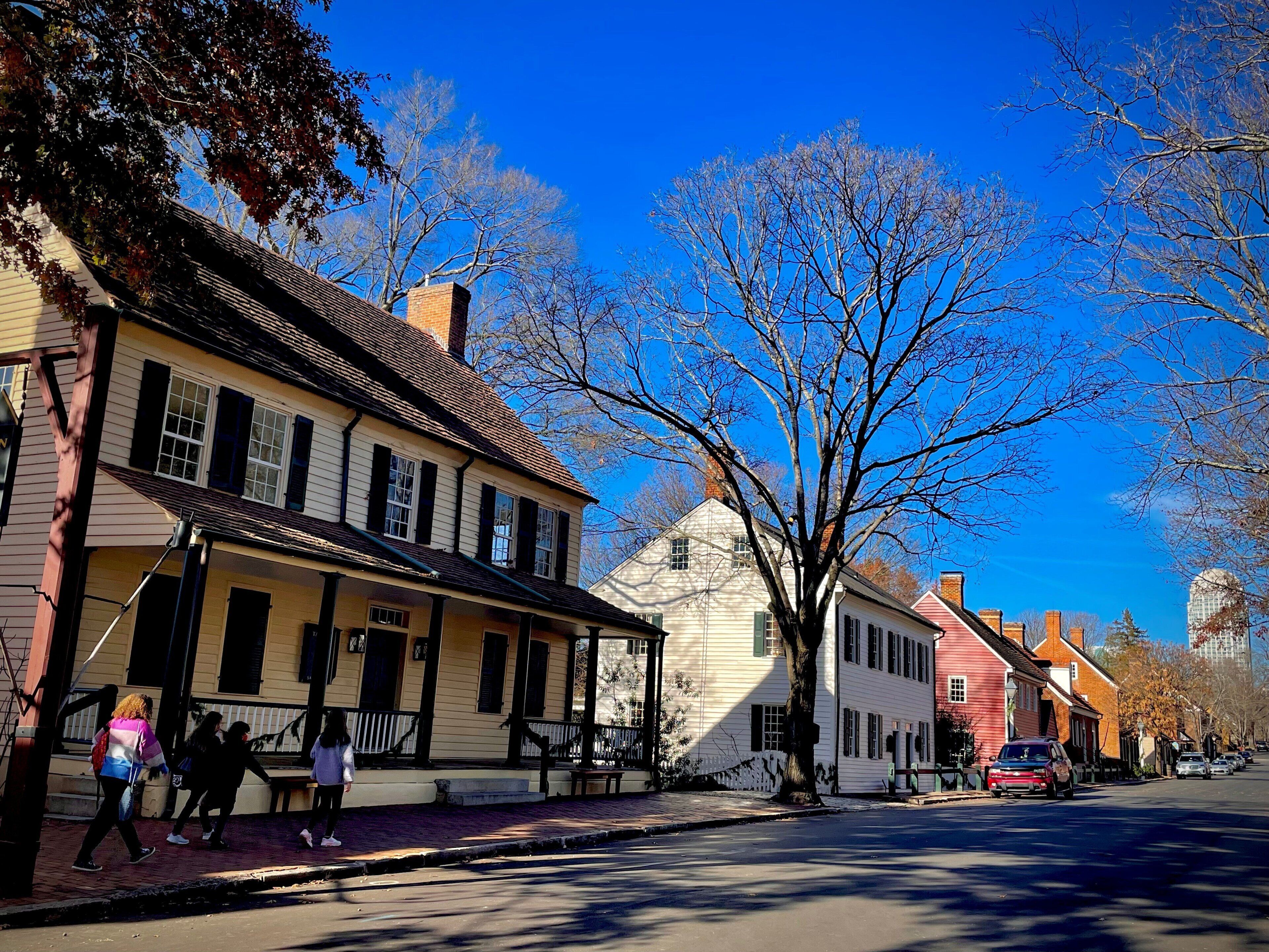 A street with historic buildings, a tree-lined sidewalk, and parked cars.