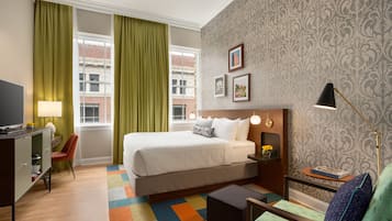 Habitación de hotel con cama, escritorio, silla, lámpara y vistas a la ciudad.