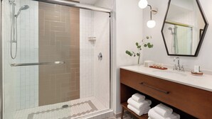 A modern bathroom with a glass-enclosed shower, a vanity with a mirror and lights, and neatly folded towels. - Hotel Indigo Winston-Salem Downtown by IHG (Winston-Salem)
