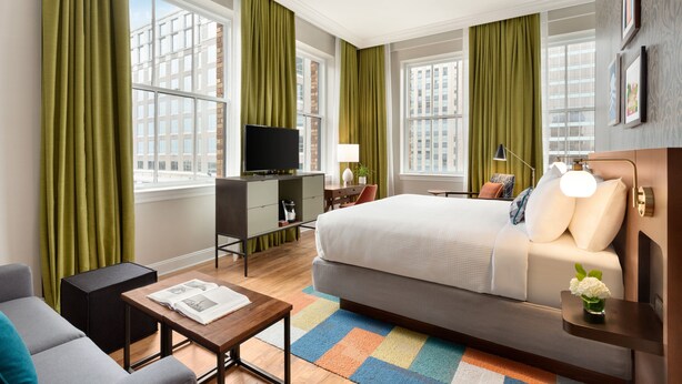 A modern hotel room with a large bed, a desk, a TV, and a view of the cityscape. - Hotel Indigo Winston-Salem Downtown by IHG (Winston-Salem)