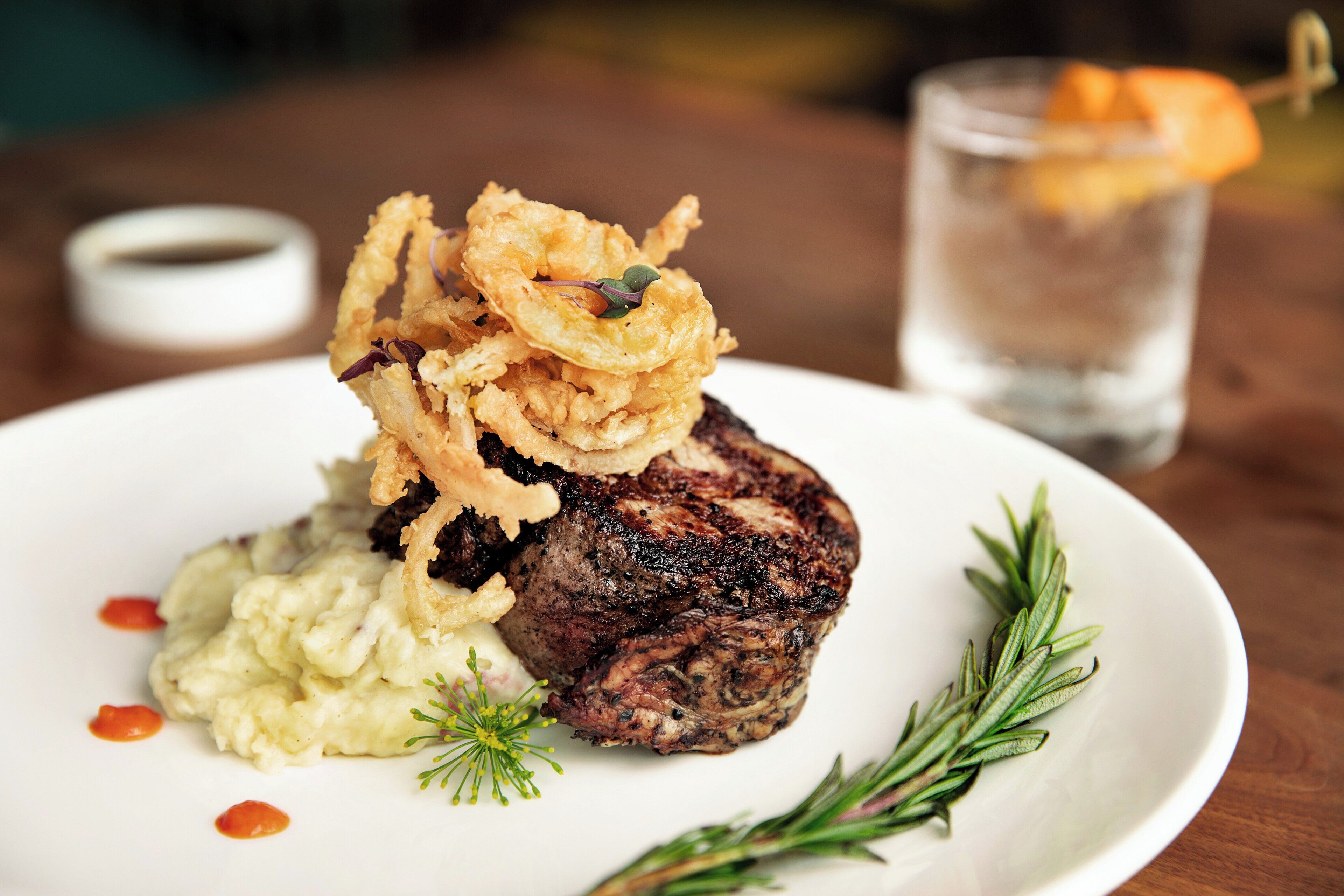 A plate with a steak, mashed potatoes, and fried onions.