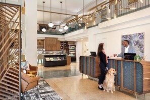 A hotel lobby with a reception desk, a staircase, and a seating area with a patterned rug.