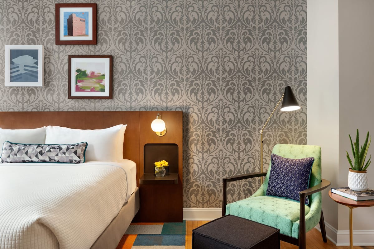 A neatly arranged bedroom with a bed, a nightstand, a chair, and a small table with a plant.