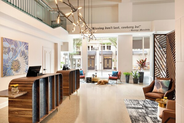 A modern hotel lobby with a reception desk, seating area, and a staircase.
