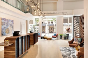 A modern hotel lobby with a reception desk, seating area, and a staircase.