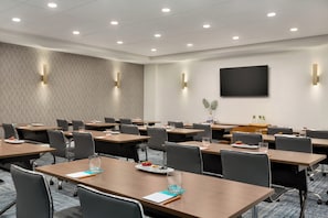 Un salón de conferencias con mesas, sillas, un televisor de pantalla plana e iluminación instalada en la pared.