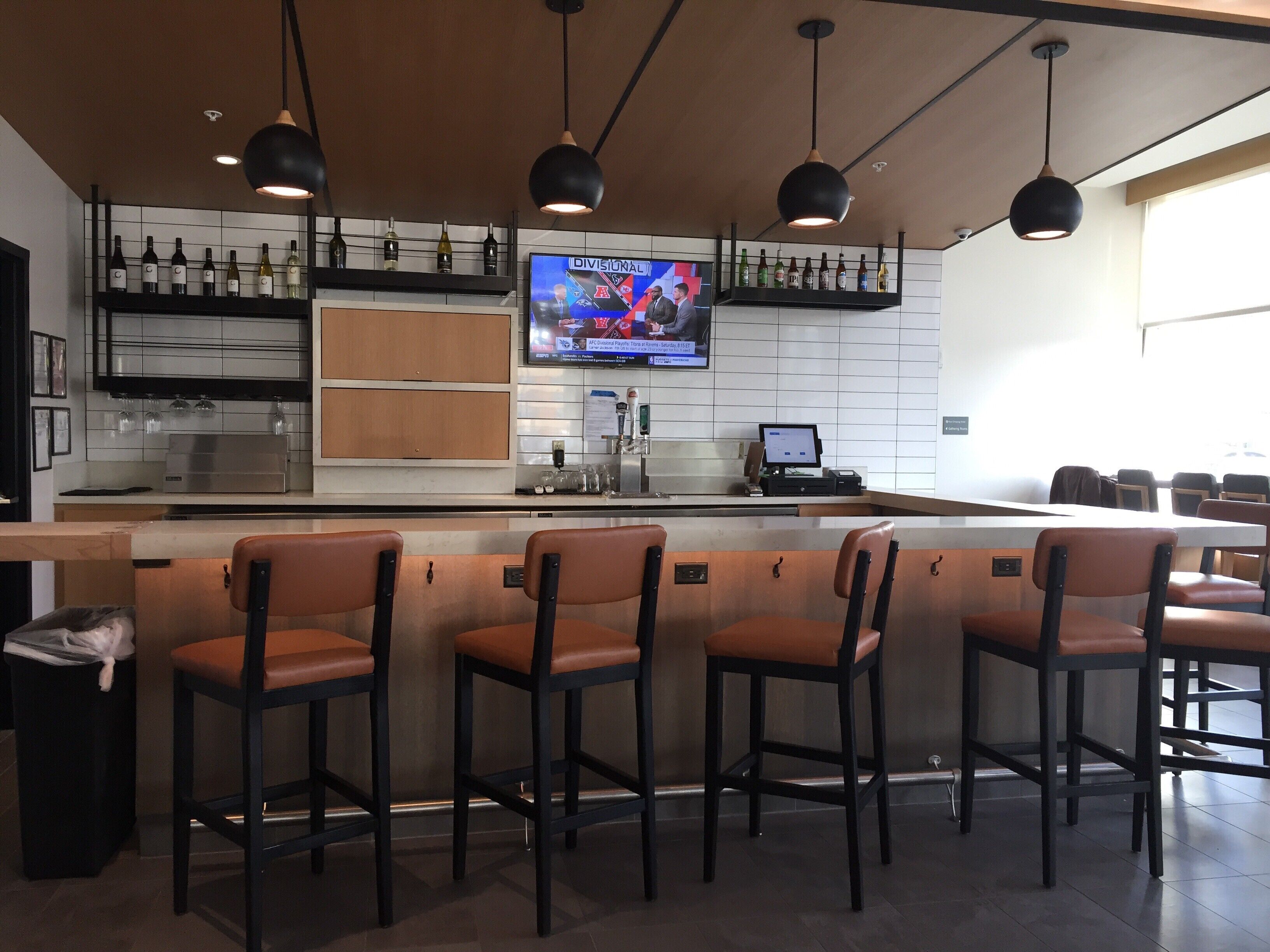 A bar area with a counter, bar stools, a television displaying a sports event, and a wine rack above the counter.