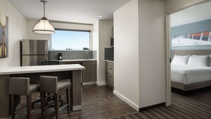 Una habitación de hotel moderna con kitchenette, zona de comedor, cama grande y vista a la ciudad.