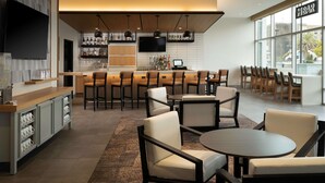 Un bar moderno con barra, taburetes y televisor. Hay varias zonas de estar con mesas y sillas.