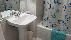 A bathroom with a white sink, a mirror, a shower curtain with a geometric pattern, and a blue towel hanging on the wall. - Rincón Do Demo (Nigran)